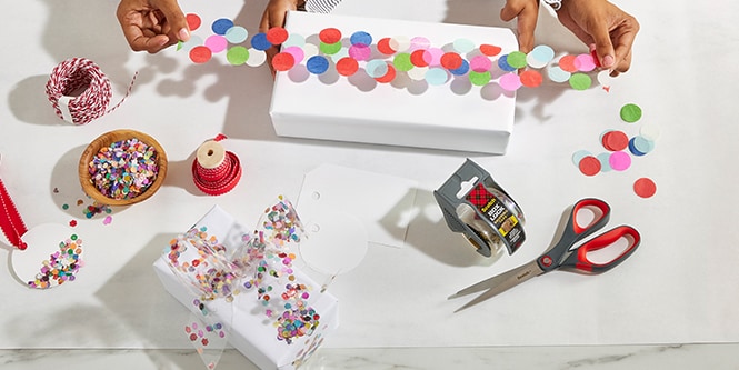 Frau und ihre Tochter verpacken eine Geschenkbox mit Konfettiklebeband, hergestellt durch das Ankleben von buntem Konfetti auf Scotch® Verpackungsklebeband

